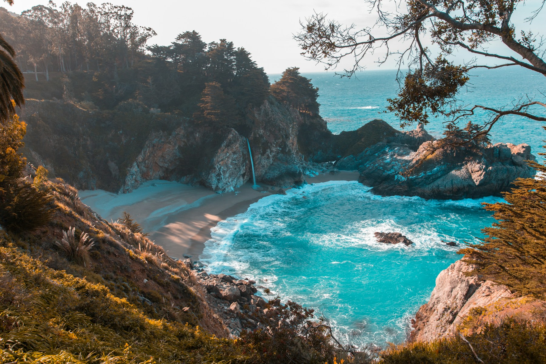 Turquoise water and a waterfall cascading into a secluded coastal cove